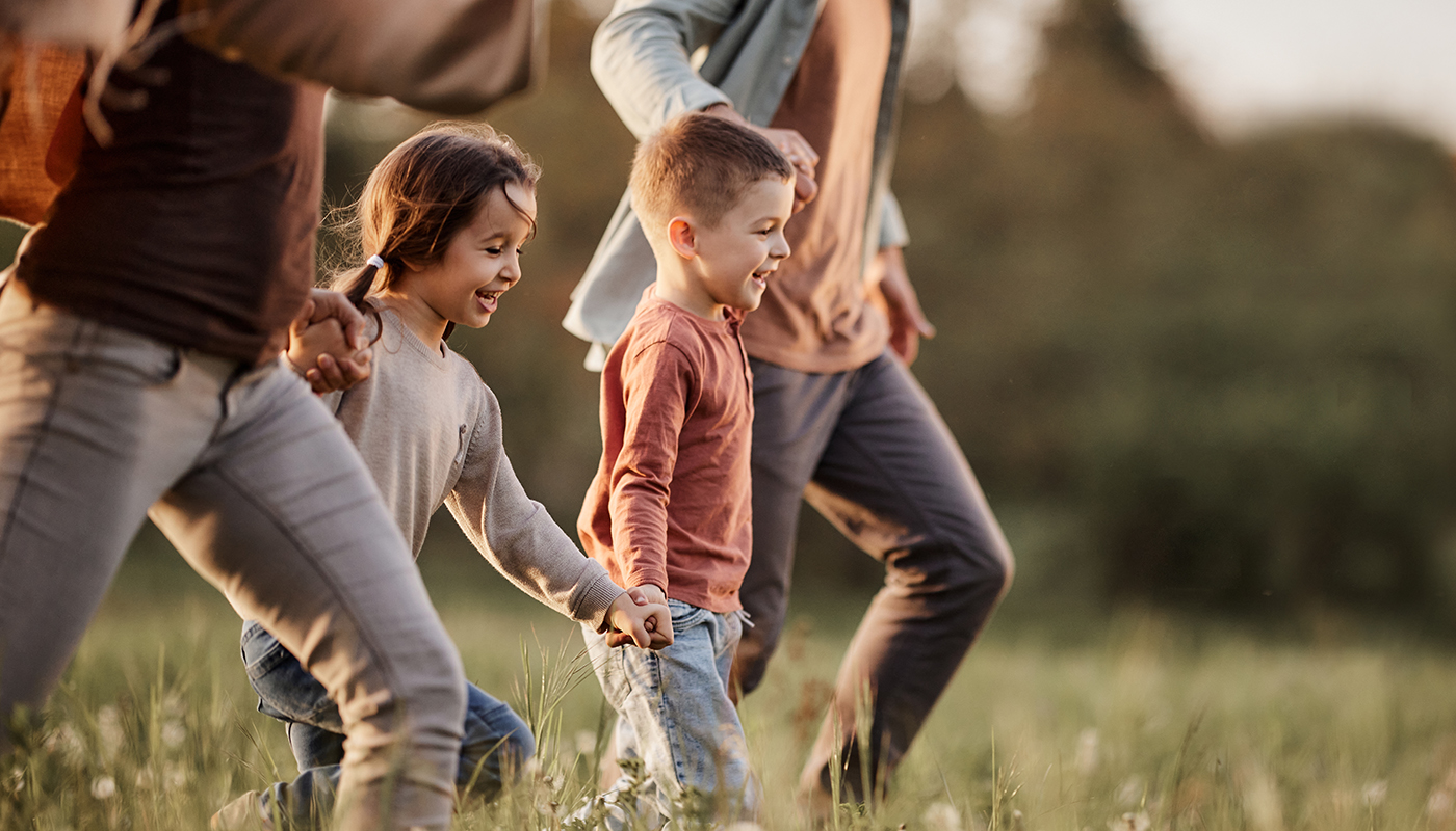 Familie mit zwei Kindern läuft Hand in Hand gut gelaunt über Wiese